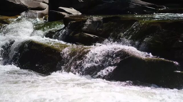 Clear water flowing over smooth rocks in a natural river rapids with white foam and spray