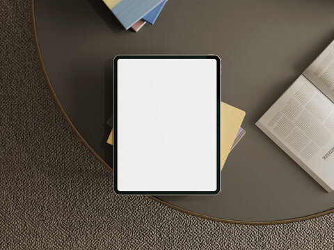 Tablet mockup on a dark modern table with books and an open magazine on a stylish interior.