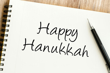 Handwritten Happy Hanukkah message on a spiral notebook with a pen, perfect for seasonal greetings and festive holiday celebrations on a wooden desk