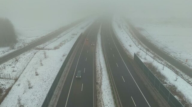 Moving cars on a winter expressway in fog captured from a drone gradually ascending upward during the recorded shot