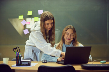 Two young women studying together with laptop in friendly classroom mood. Concept of education content, teamwork visuals, learning materials, youth branding, and school lifestyle storytelling.