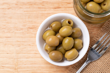 Pickled olives, Pitted green olives in a bowl and glass jar on wooden background, Table top view