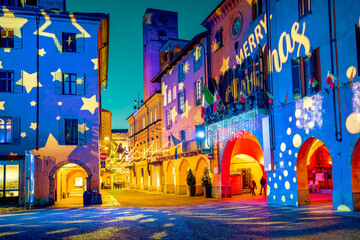 A street and historic buildings of Alba, Italy, illuminated by colorful light projections during a Christmas holidays at twilight.