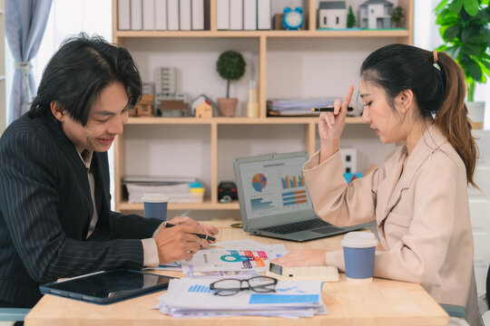 Asian business couple discussing finances over documents and laptop, explaining details of business growth chart.