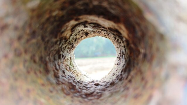 Old iron metal dirty sewer or drainage round pipe hole inside view with rust, corrosion and weathering damage. Aged bore well, sewage pipeline or rusty tube concept.