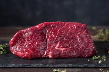 Chop of boneless red meat beef on black slate board with spices and condiments for cooking
