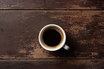 Espresso coffee in white porcelain cup on old wooden table, top view