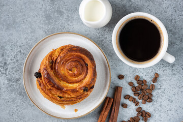 Raisin cinnamon swirl puff pastry bun and cup of black coffee on stone background, top view. Coffee break