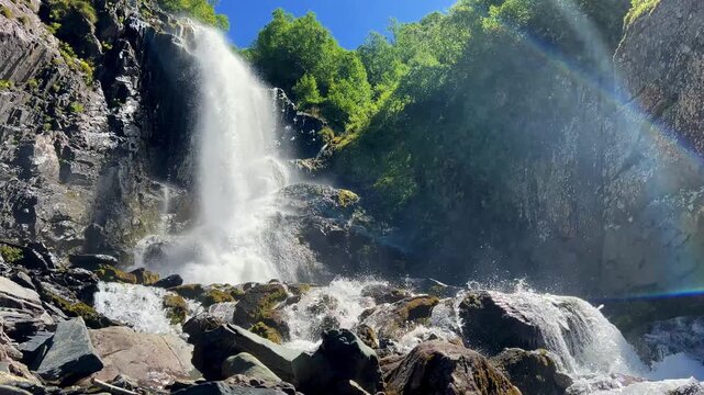 Dombai-Ulgen Gorge, Chuchhur waterfall is framed by malachite greenery of grasses and dense forests. A waterfall flowing down from a glacier. A two-stage stream with white foam, near the Chuchhur pass
