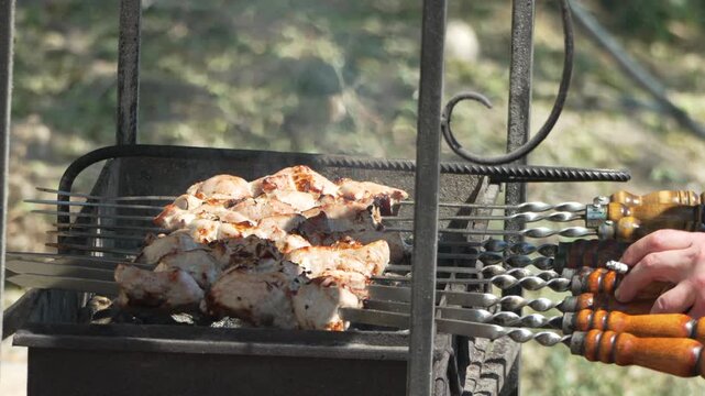 Grill meat cooking shashlik being rotated on an outdoor brazier during a summer picnic