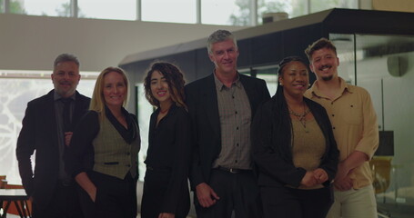 Diverse group of six professionals smiling in modern office space, business team standing together in bright indoor environment with friendly relaxed posture