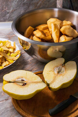 A quince cut in half a wooden board and next to it is a bowl with quince peelings and a metal bowl with peeled quince. 