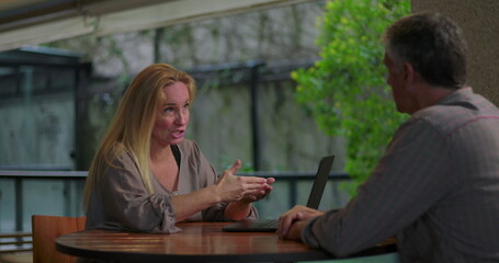 Female professional explaining idea to male coworker during team meeting in open office setting with laptop on table