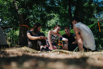 A group of friends camp in a shaded park, sharing a playful moment stacking colorful blocks while chatting and laughing. A relaxed, social outdoor scene focused on teamwork and leisure.