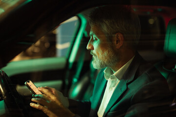 Mature man focused on smartphone in parked car at night