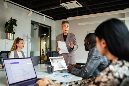 Mature woman presenting to focused team in modern office
