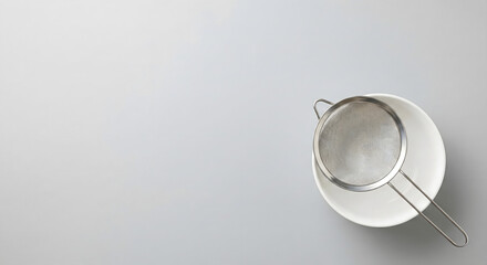 Stainless steel sifter on a white bowl for baking on grey background.