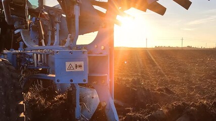 Tractor with agricultural machinery cultivates the arable land at sunset and prepares the soil for sowing agricultural crops, slow motion. Beautiful rural landscape