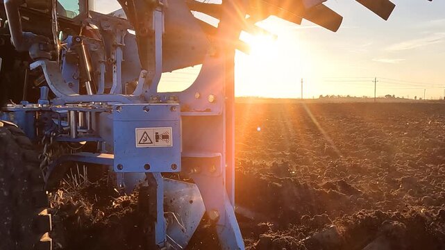 Tractor with agricultural machinery cultivates the arable land at sunset and prepares the soil for sowing agricultural crops, slow motion. Beautiful rural landscape