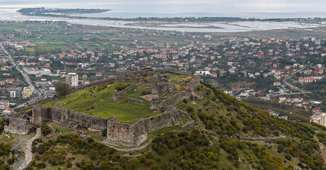 Aerial view of Lezh&euml; Castle&rsquo;s ruins on the hillside, overlooking the town, fields, and wetlands near the Adriatic coast.
