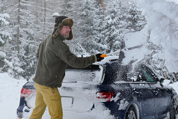 Man clearing thick snow from car during severe winter weather with trees in background