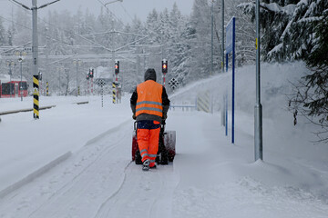 Worker operating a snow blower to clear pathways at a railway station covered in snow