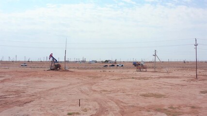 aerial oil pumpjack on flat desert field, slow mechanical motion, sparse poles and distant units, dusty red earth and pale sky, industrial extraction scene with wide perspective and working wells