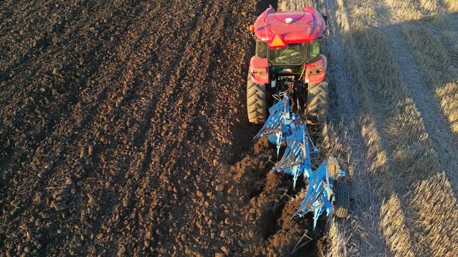 Aerial view of tractor with agricultural machinery cultivates the arable land and prepares the soil for sowing agricultural crops. Drone footage of a tractor plowing the land, rural landscape