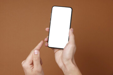 Man holding smartphone with blank screen on brown background, closeup. Mockup for design