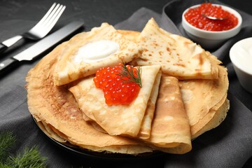 Delicious crepes with red caviar and sour cream on black table, closeup
