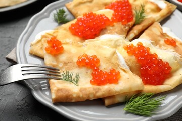 Tasty crepes with red caviar and sour cream on black table, closeup