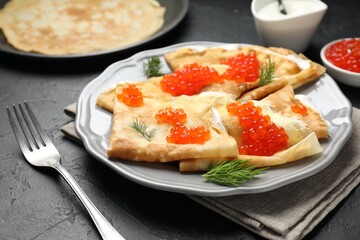 Tasty crepes with red caviar and sour cream on black table, closeup