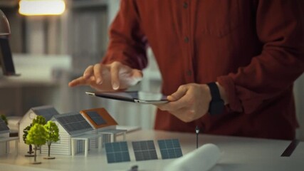 An engineer is focused on a touchpad, evaluating solar panel layouts in a modern workspace filled with models. The setting showcases innovation in renewable energy technologies