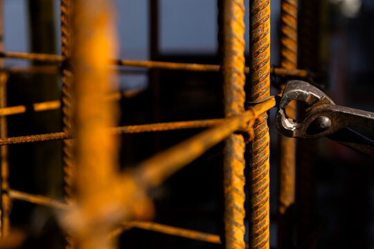 Close-up of a construction worker wearing protective gloves and using pliers to cut or tie steel rebar at a job site. Warm light highlights the texture of rusted metal and manual labor.
