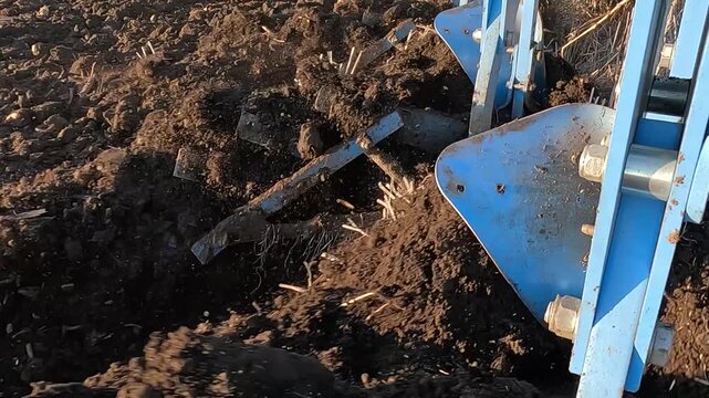 Tractor with agricultural machinery cultivates the arable land and prepares the soil for planting crops. Close up of a tractor plowing the land. The plow cuts the soil and turns it over, slow motion