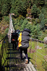 Nepalian Porter carrying heavy load on his back going along the bridge to Everest Base camp....