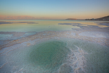 Abstract, high-contrast view of the Dead Sea shoreline, featuring intricate, crystalized white salt formations meeting the strikingly unnatural green water