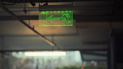 A bright green exit sign is visible indoors, directing individuals toward the exit. The sign features a figure running and an arrow pointing left, ensuring easy navigation during emergencies - Powered by Adobe