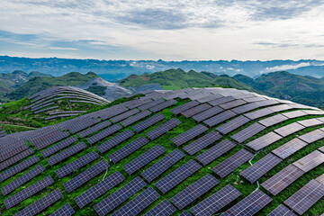 Solar panels covering the green mountain slopes under blue sky.