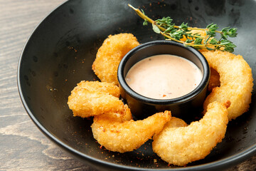 Golden-fried, breaded popcorn shrimp with a creamy dipping sauce in a black bowl, garnished with fresh thyme on a wooden table