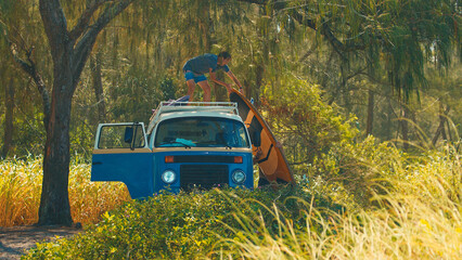 Two men unload surfing boards from the roof of the classic retro bus. Modern hippies travel by retro bus in a search of perfect waves in Brazil