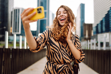 Selfie time! Young woman is enjoying herself with phone in bustling cityscape. Beautiful tourist...