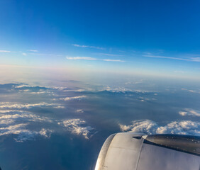 Breathtaking aerial view above layered clouds and mountains from airplane window with engine cowling visible during high altitude commercial flight.