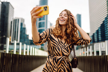 Selfie time! Young woman is enjoying herself with phone in bustling cityscape. Beautiful tourist...