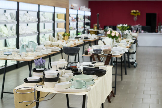 Ceramic tableware and kitchenware arranged on display tables in modern store showroom, various plates, bowls, cups, and decorative items organized for retail presentation