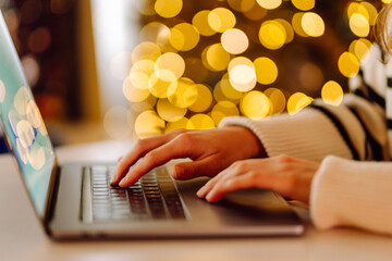 A close-up of a young female freelancer's hands typing on a laptop in a decorated room. Human hands...