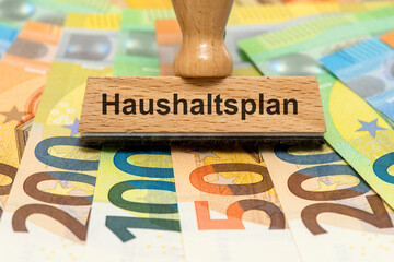 Ein Holzstempel ist beschriftet mit dem Aufdruck Haushaltsplan als Symbolbild f&uuml;r Planung und Konzeption eines Finanzplans f&uuml;r den Haushalt - digital bearbeitet