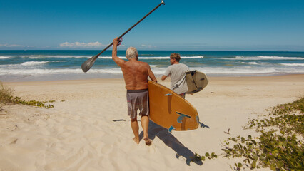 Young and elderly surfers walk with surfing boards on the beach in Brazil