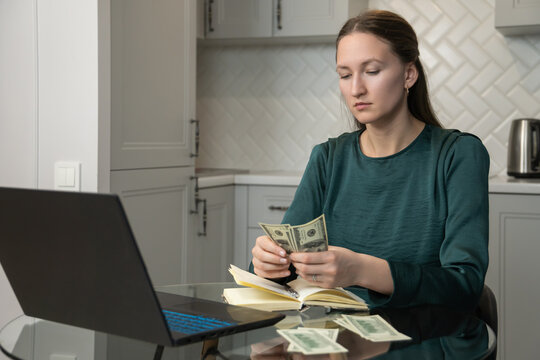 Businesswoman sitting at glass desk in home office, counting us dollar banknotes, with laptop and notebook nearby, managing home finances, budgeting, or calculating investment returns - Powered by Adobe