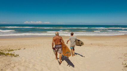Young and elderly surfers walk with surfing boards on the beach in Brazil